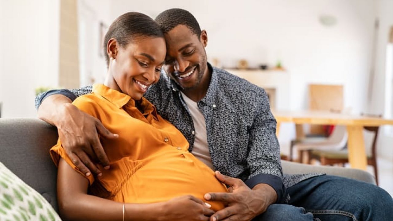 Black expectant parents sitting on sofa dreaming about their baby