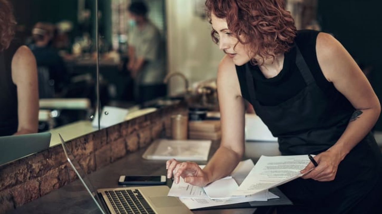Shot of an attractive young hairdresser standing and using her laptop while calculating her finances in her salon