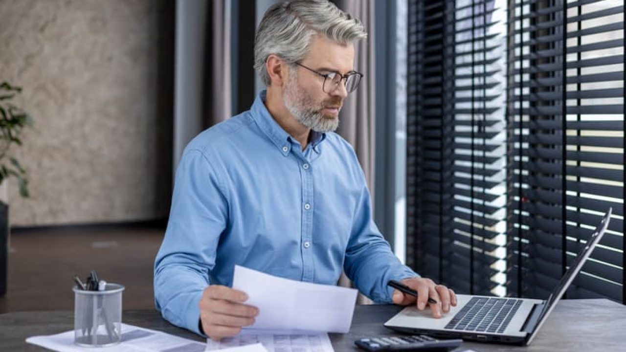 Mature businessman working on laptop at desk in office environment