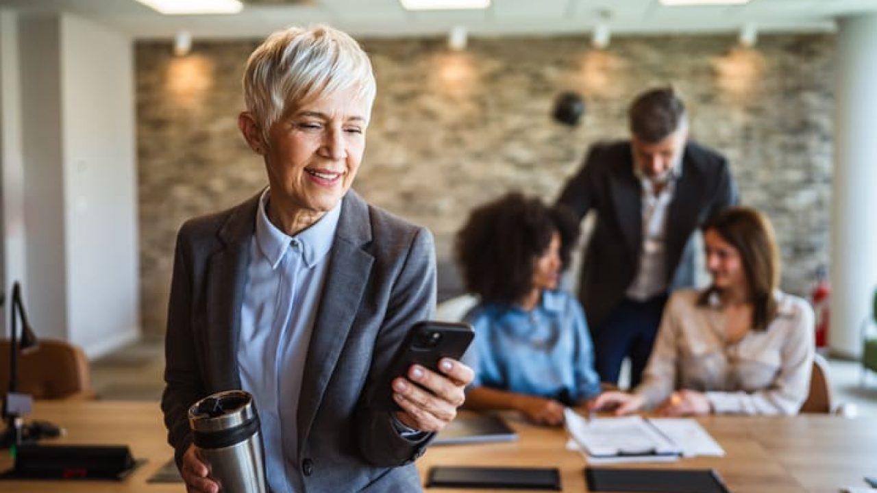 aged businesswoman use mobile phone and drink coffee at workplace