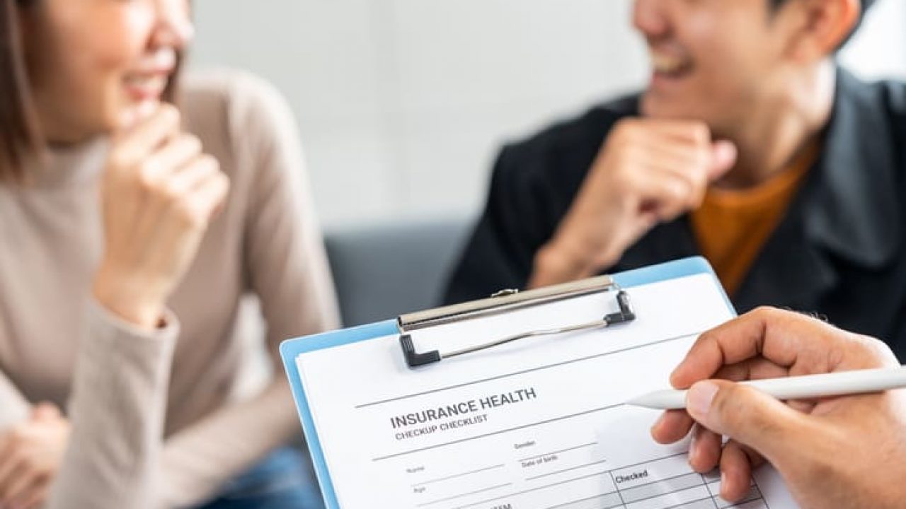 A young couple discusses life health and home insurance plans with an advisor ready to sign documents for future security and peace of mind. Meets with an insurance agent to review and sign policies