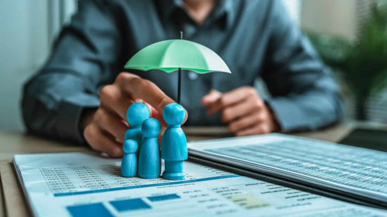 A wooden doll under an umbrella holding by agent represent insurance . Family , protection, life.